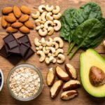 Variedade de alimentos ricos em magnésio sobre superfície de madeira rústica incluindo sementes de abóbora amêndoas castanhas chocolate amargo espinafre feijão preto aveia abacate banana e brócolis